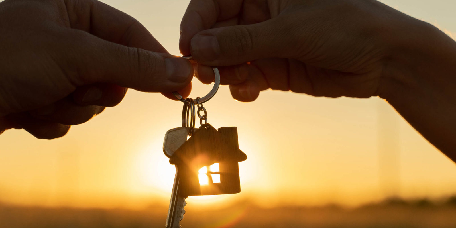 Frau gibt Mann den neuen Hausschlüssel, im Hintergrund ein Sonnenuntergang